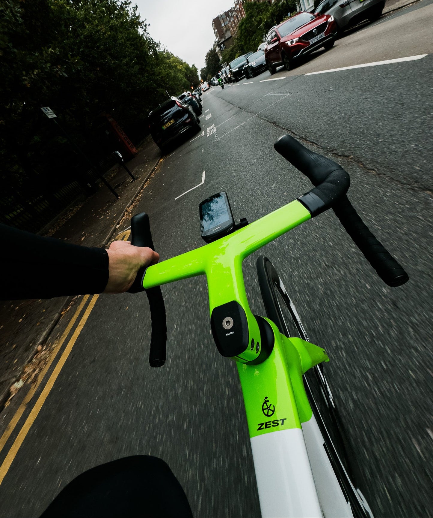 Person riding a green and white electric bike on a city street with cars and trees in the background.
