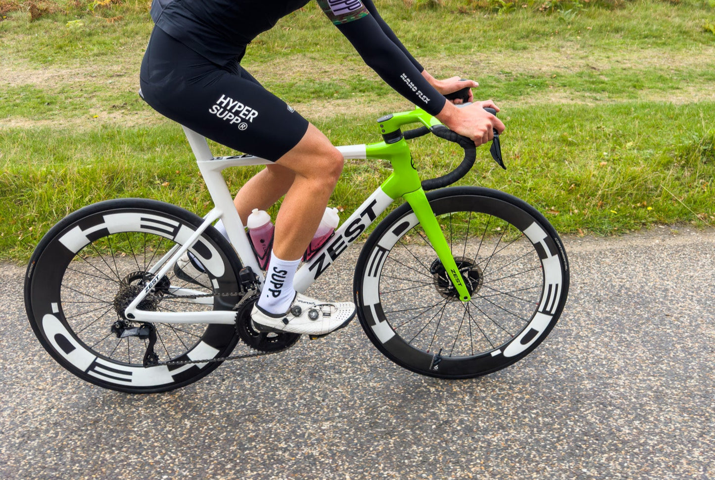 Person riding a green and white bicycle on a road with grass and trees in the background